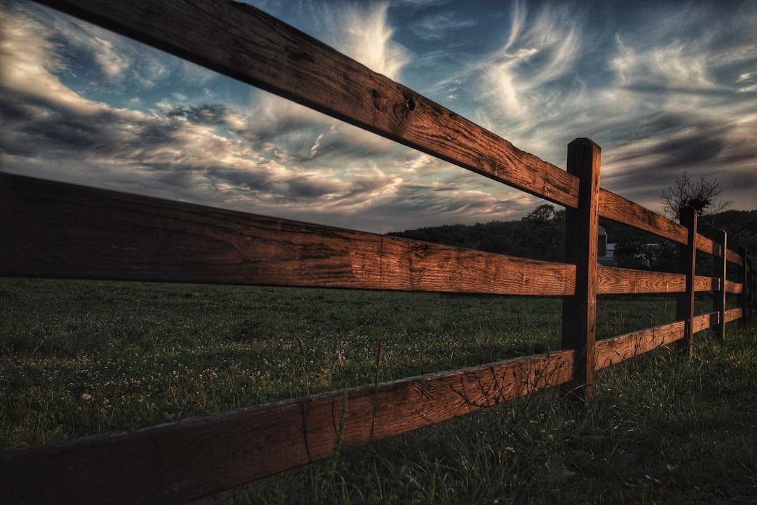 A weathered wooden fence runs through a grassy field with distant hills.